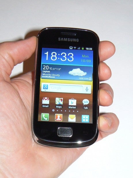 Hand holding Samsung Galaxy Mini 2 smartphone displaying home screen.
