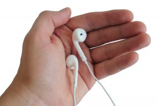 Hand holding a pair of white Apple EarPods.