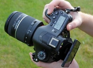 Hands holding Sony Alpha A99 DSLR with lens and screen open.