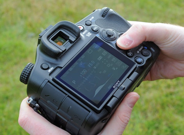 Hands holding a Sony Alpha A99 camera displaying settings screen.