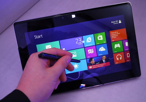 Asus Taichi laptop with stylus on touchscreen displaying Windows interface.