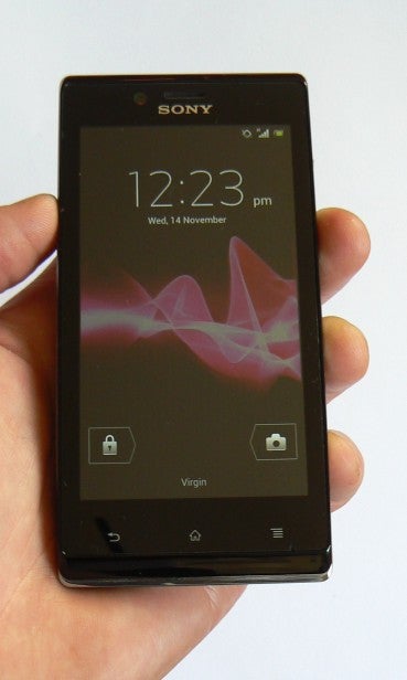 Hand holding Sony Xperia J smartphone displaying time and date.