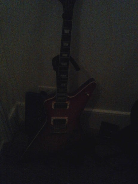 Red electric guitar leaning against a wall in dim lighting.