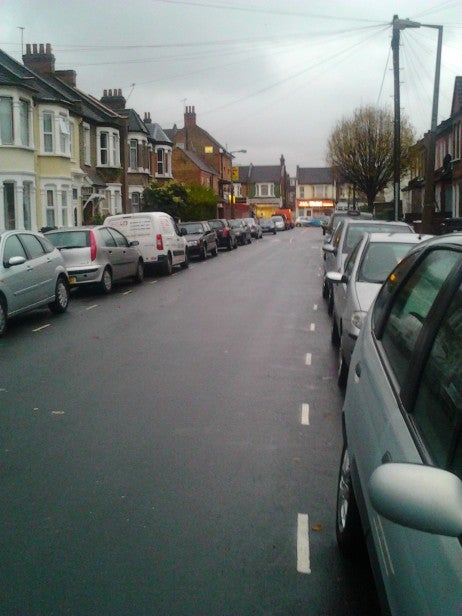 Residential street with parked cars and an overcast sky.