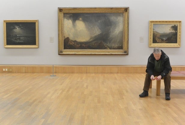 Man sitting in gallery with landscape paintings on wall.