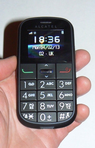Hand holding an Alcatel mobile phone displaying home screen.