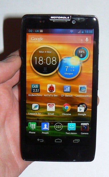 Hand holding a Motorola smartphone displaying home screen and apps.