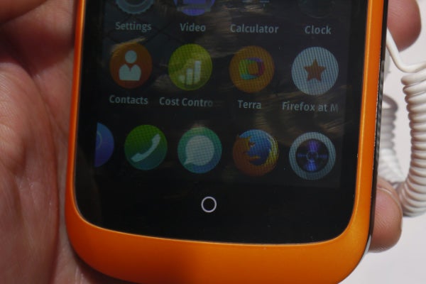 Hand holding a Firefox OS smartphone displaying various apps.
