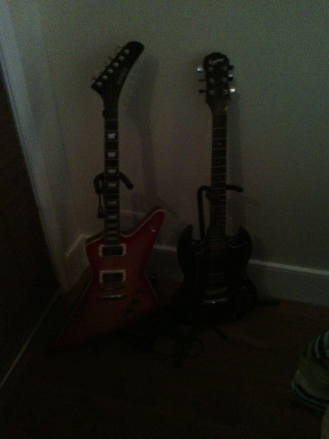 Low-light test shot of two electric guitars leaning against a wall.