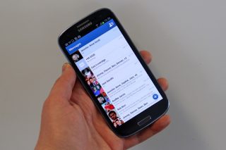 Samsung smartphone displaying Facebook Home interface in hand.