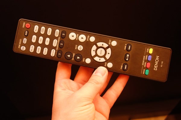 Hand holding a Denon AVR-X2000 remote control.