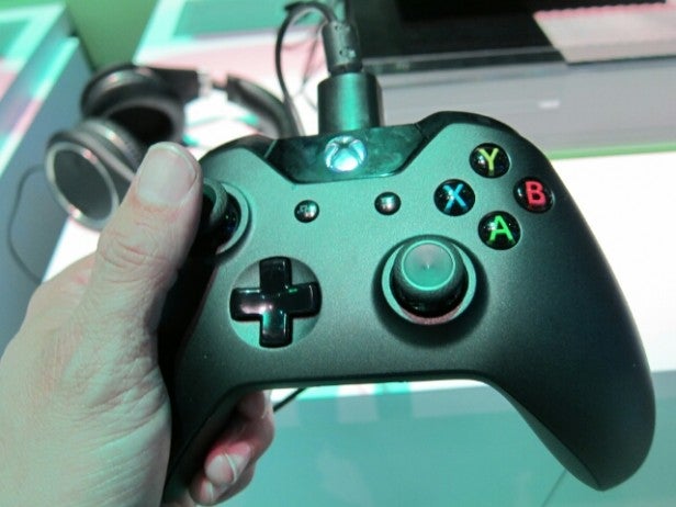 Hand holding a black Xbox One controller with green backlighting.Hand holding a black Xbox One controller with glowing buttons.