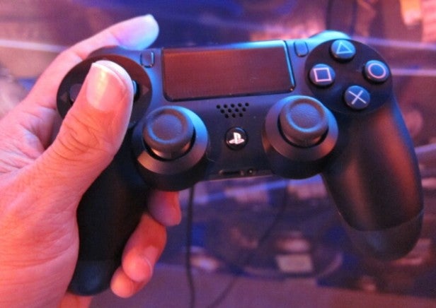 Hand holding a black DualShock 4 controller.