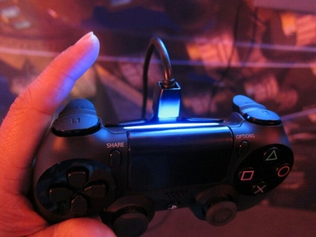 Hand holding a glowing DualShock 4 controller in low light.