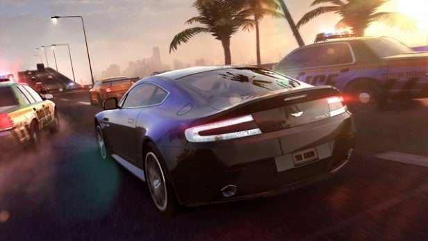 Screenshot of The Crew racing game with cars and cityscape.Black sports car chased by police in a video game scene.