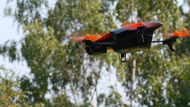 Drone in flight against a backdrop of trees.