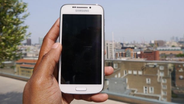 Hand holding a Samsung smartphone with city skyline in background.