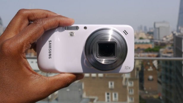 Hand holding a Samsung camera with cityscape in the background.