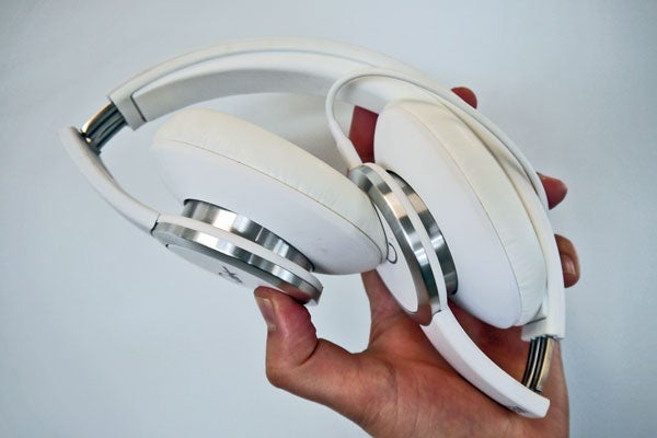 Hand holding WeSC Chambers by RZA white headphones.