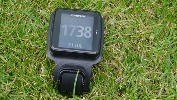 TomTom Runner GPS watch on grass displaying time and date.TomTom Runner GPS watch displaying time on grass.
