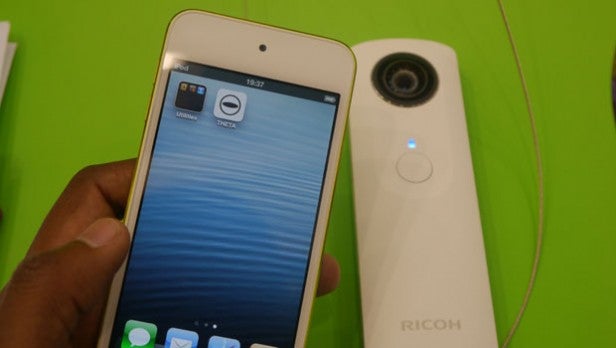 Ricoh Theta camera next to a smartphone with app open.