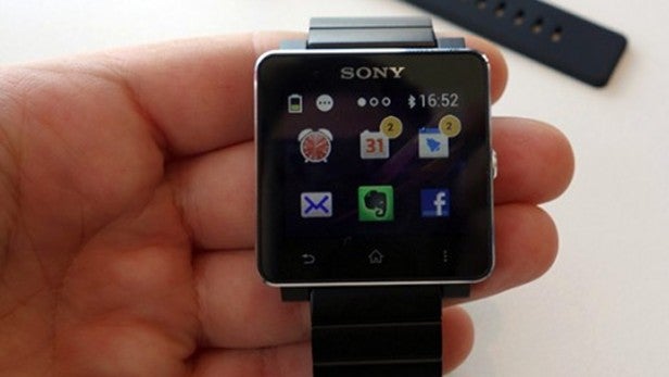 Hand holding Sony smartwatch displaying time and app icons.