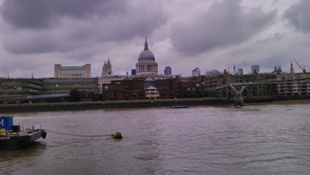 Photo of cloudy skyline over river with city buildings.