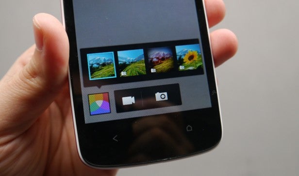 Hand holding a smartphone displaying camera interface with photos.