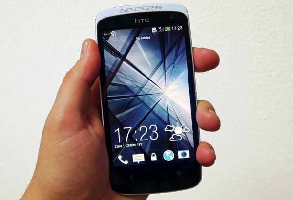 Hand holding an HTC Desire 500 smartphone displaying home screen.