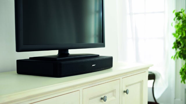 Bose Solo soundbar placed under a flat-screen TV on a white stand.
