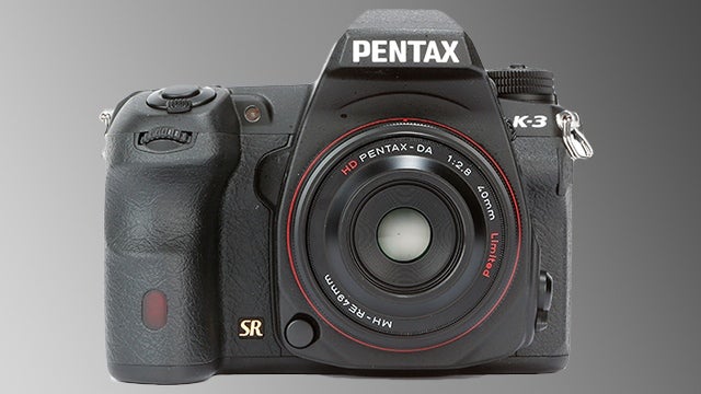 Pentax K-3 DSLR camera with HD lens on gray background.