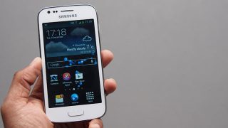 Hand holding a Samsung Galaxy Ace 3 showing home screen.