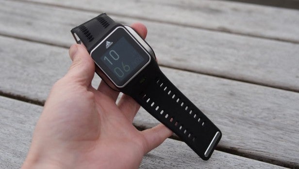 Adidas miCoach Smart RunHand holding a smartwatch showing time on wooden surface.