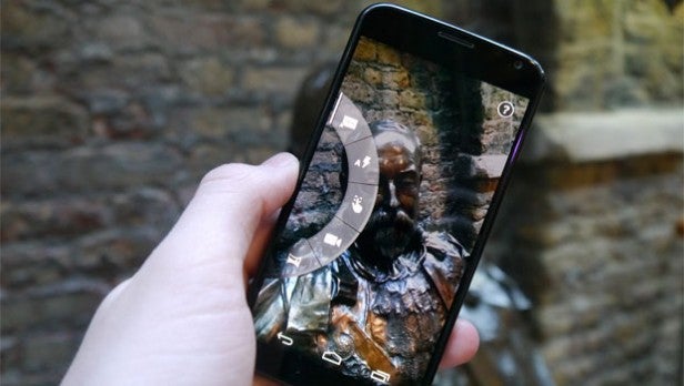 Smartphone in hand displaying camera interface with statue photo.