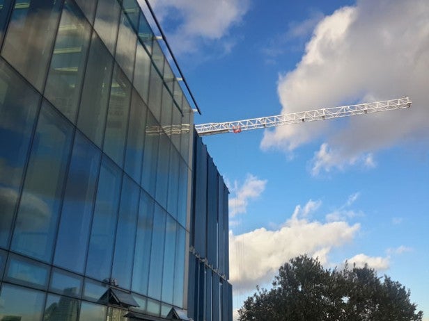 Glass building and construction crane against a cloudy sky.