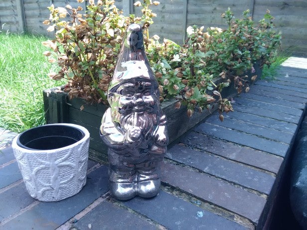 Silver garden gnome statue on a brick patio with plants.