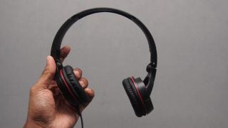 Hand holding Pioneer SE-MJ532-R black and red headphones.