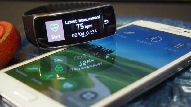 Fitness tracker displaying heart rate measurement beside smartphone.