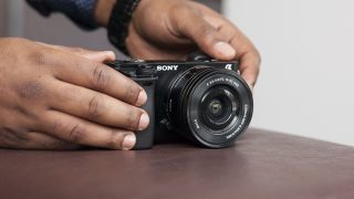 Person holding a Sony A6000 camera on a table.