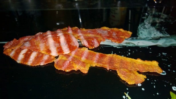 Three strips of crispy bacon on a reflective surface