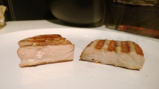 Two slices of cooked pork belly on a white plate.