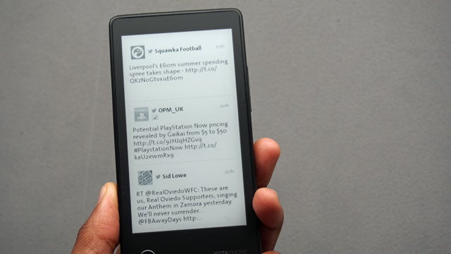 Hand holding YotaPhone displaying Twitter feed on e-ink screen.