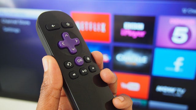 Hand holding Roku Streaming Stick remote with TV interface in background