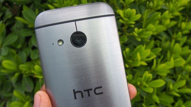HTC smartphone held in hand with camera visible against greenery background.