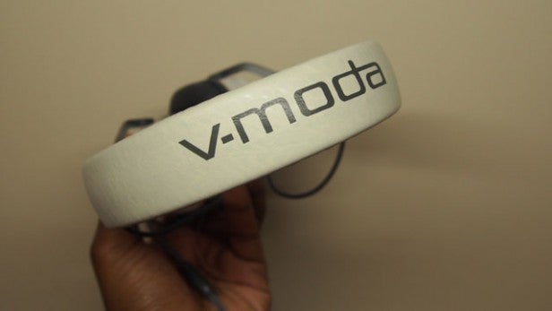 Hand holding V-Moda XS headphones with logo visible.