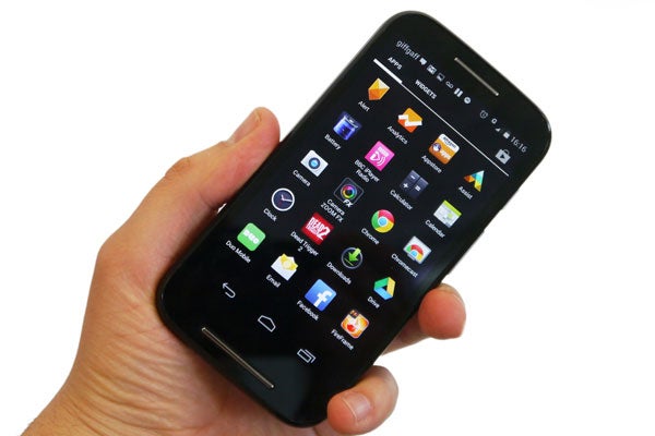 Hand holding a Motorola Moto E displaying apps on screen.