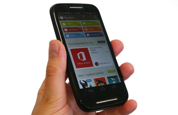 Hand holding a Motorola Moto E smartphone displaying apps.