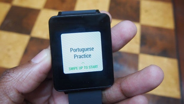 Hand holding an Android smartwatch showing a language practice app.