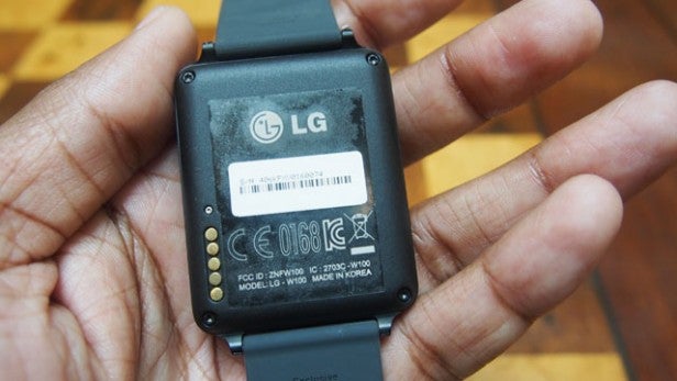 Hand holding an LG G Watch showing its back cover and model information.