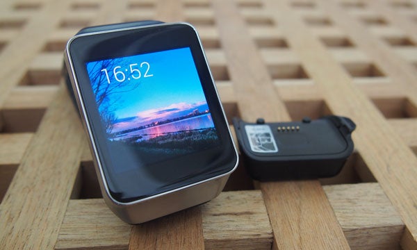 Samsung Gear Live smartwatch with charging cradle on wooden surface.